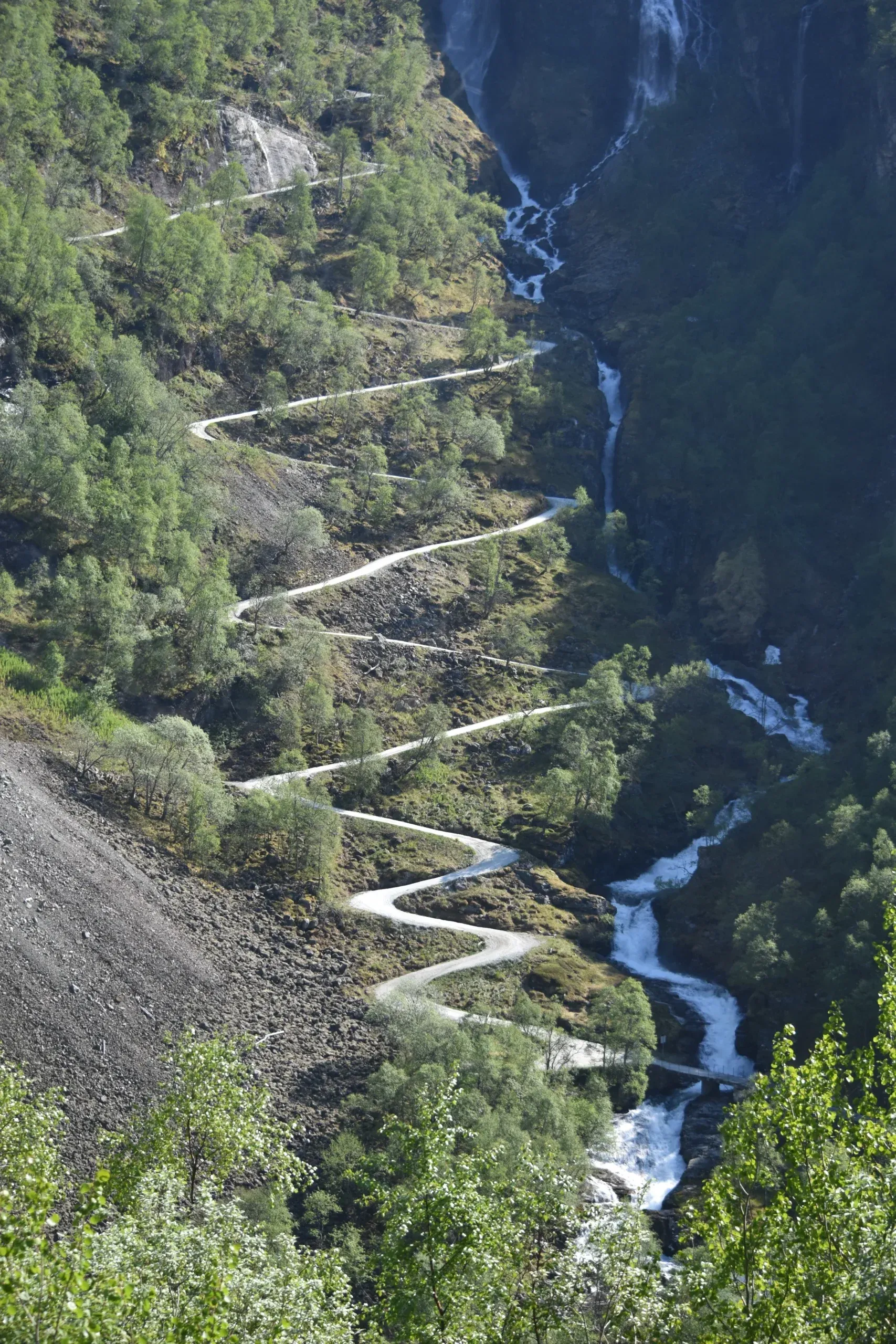 A railway line and switchback road climbing a steep green valley near Flåm, Norway.