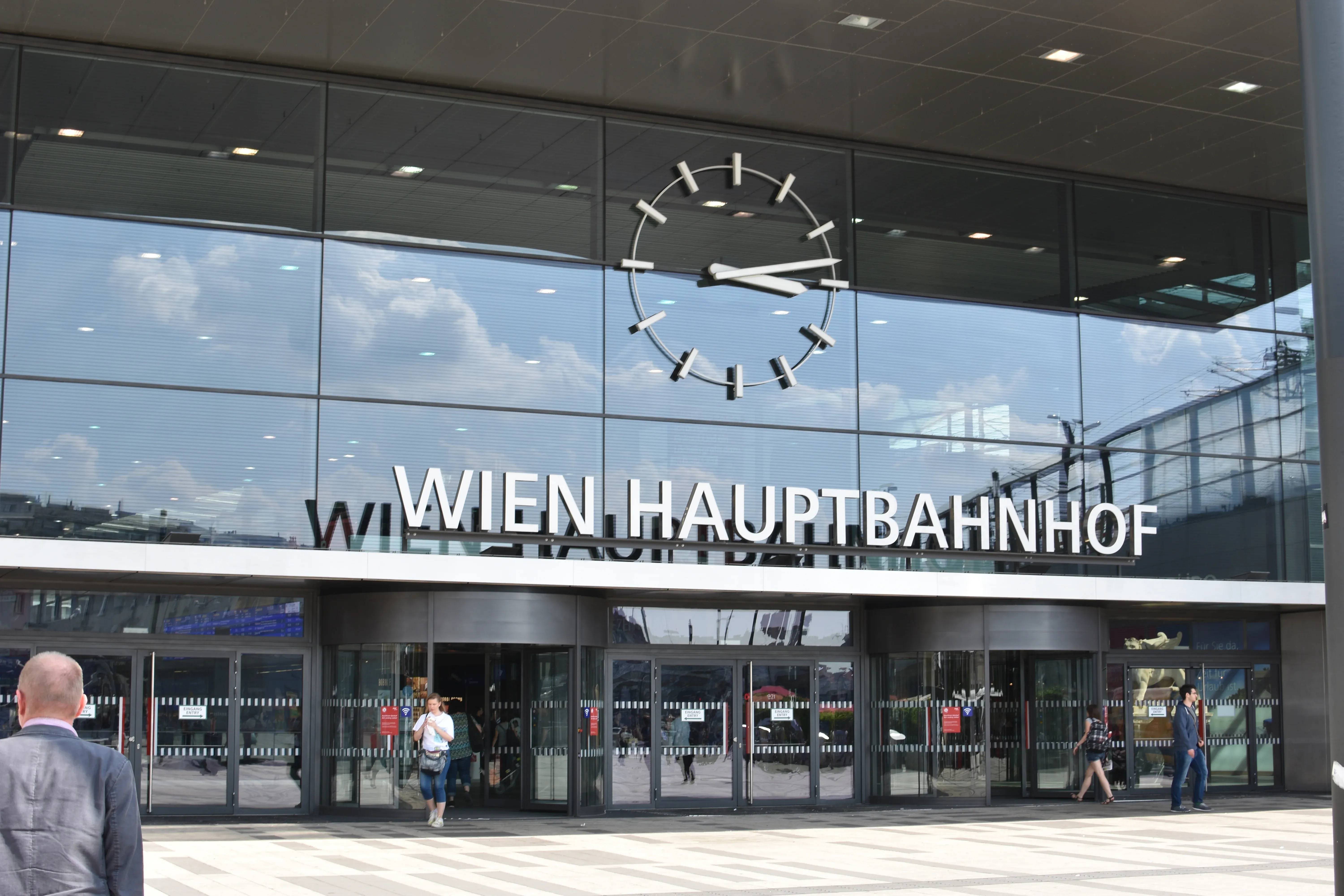 The modern glass facade of Vienna Central Station (Wien Hauptbahnhof) in Austria featuring a prominent minimalist round station clock and revolving entrances.