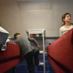 A young boy climbing a ladder to an upper bunk in a sleeper compartment on an ÖBB Nightjet train in Hamburg, while his sister sits on the other bunk.